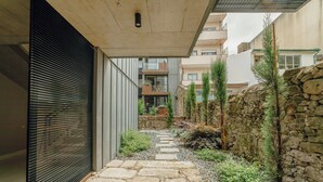 Een smal stenen pad dat leidt naar een modern gebouw met een metalen rolsluiting, omringd door groen en stenen muren.