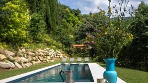 Un tavolo a bordo piscina con una caraffa, una tazza e un piatto di biscotti, immerso nel verde e affacciato su una piscina cristallina.