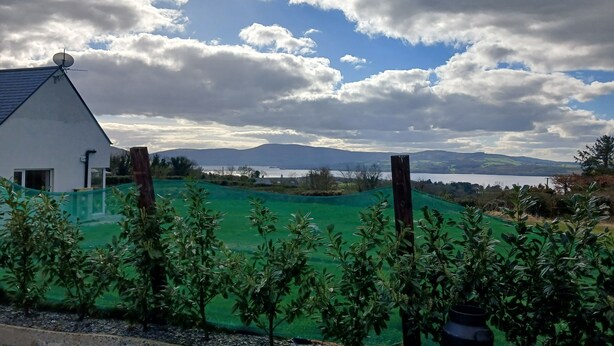 A house with a sloped roof and a satellite dish, surrounded by green fields and a body of water in the distance. - Lakeview Retreat (Garrykennedy)