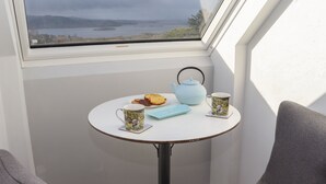 A small round table with a teapot, a mug, and biscuits by a window overlooking a lake. - Lakeview Retreat (Garrykennedy)