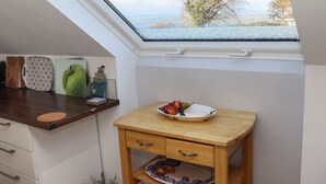 A kitchen with a skylight, a wooden table with a plate of fruit, and a white cabinet with drawers. - Lakeview Retreat (Garrykennedy)