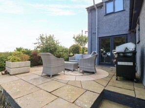 An outdoor patio with wicker furniture and a barbecue grill. - Tyn Rallt (Bodorgan)