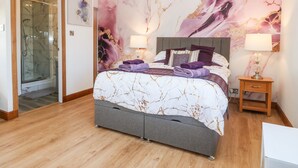Ein Schlafzimmer mit einem großen Bett, einem Nachttisch, einer Duschkabine aus Glas und einer Wand mit Marmoroptik.