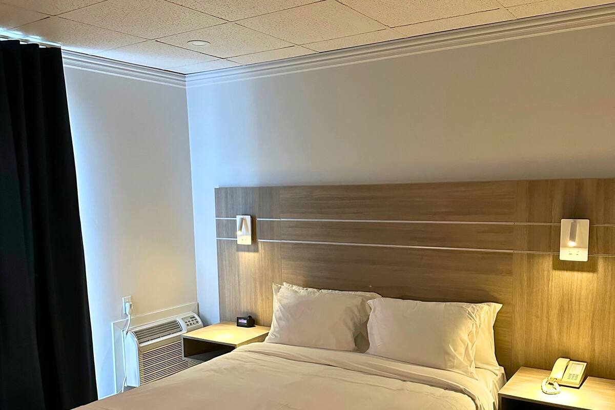Habitación de hotel con una cama grande, mesitas de noche, teléfono y un calentador de pared.