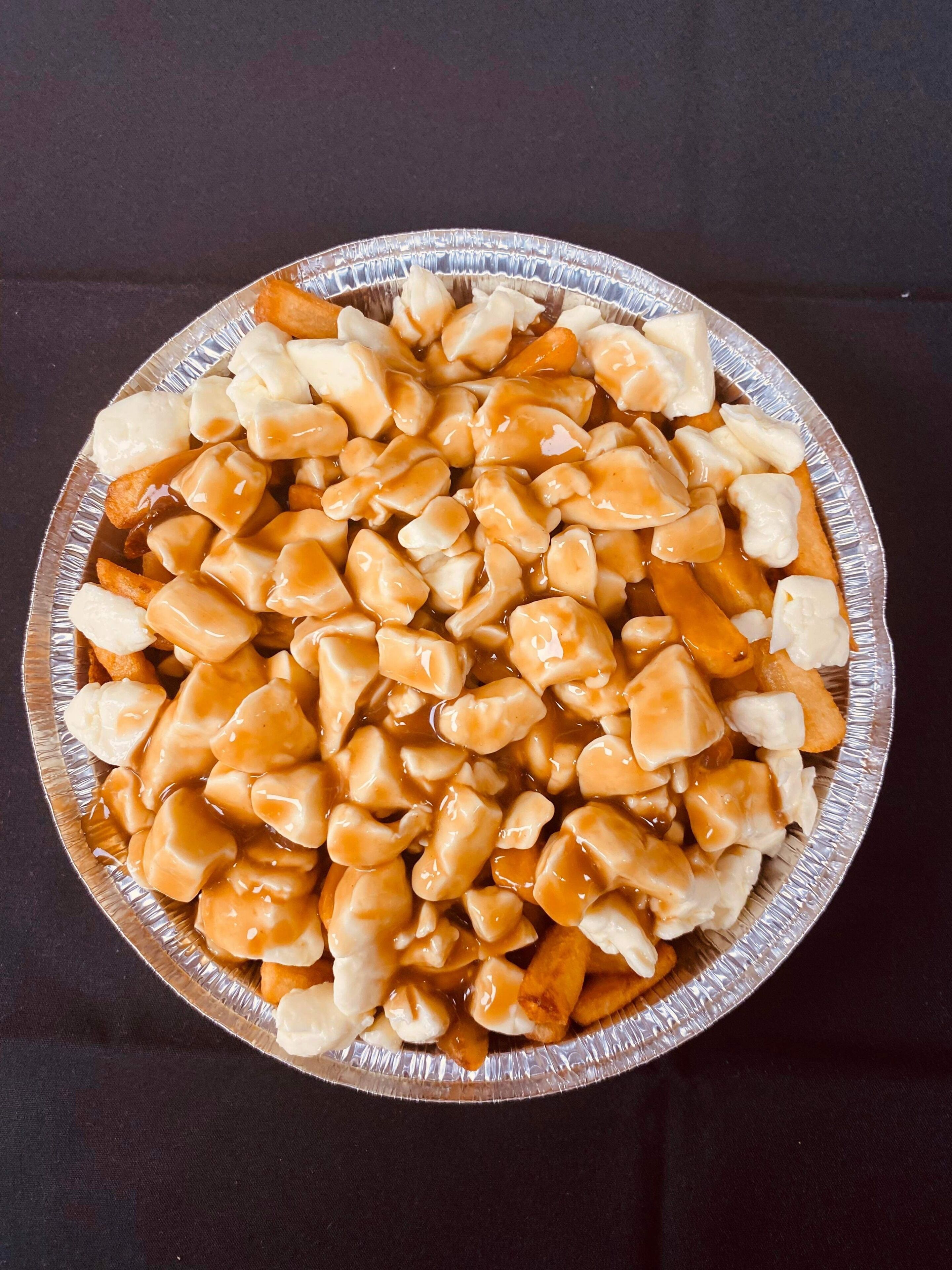 A round aluminum tray filled with poutine, a dish consisting of fries, cheese curds, and gravy.