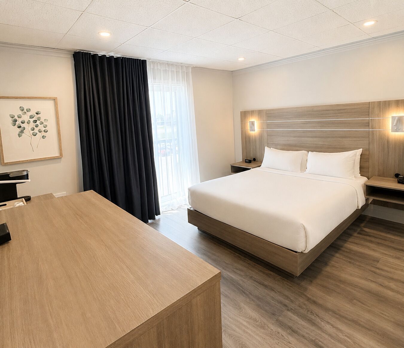Una habitación de hotel con una cama grande, mesitas de noche, un escritorio y una ventana con cortinas.