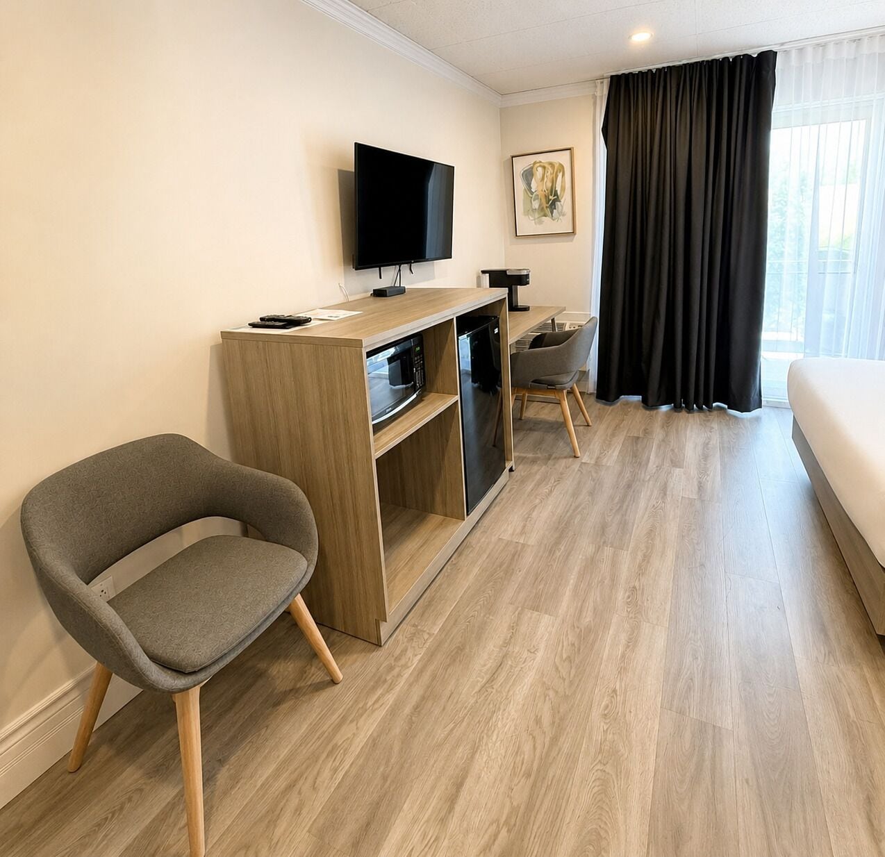 A hotel room with a bed, a TV mounted on the wall, a desk with a microwave, and a chair.