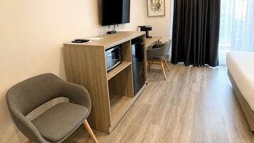 A hotel room with a bed, a TV mounted on the wall, a desk with a microwave, and a chair.