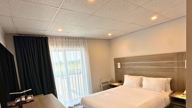 Habitación de hotel con una cama grande, un escritorio y vistas al exterior a través de una ventana con cortinas.