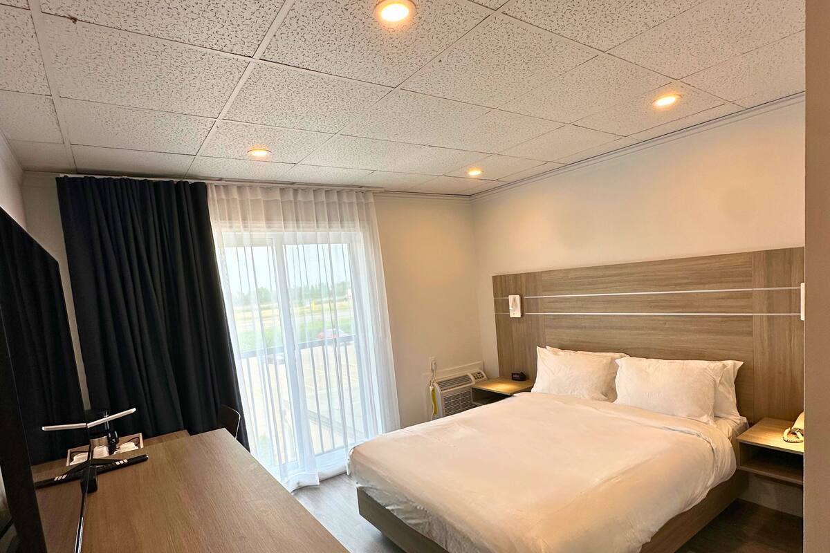 Habitación de hotel con una cama grande, un escritorio y vistas al exterior a través de una ventana con cortinas.