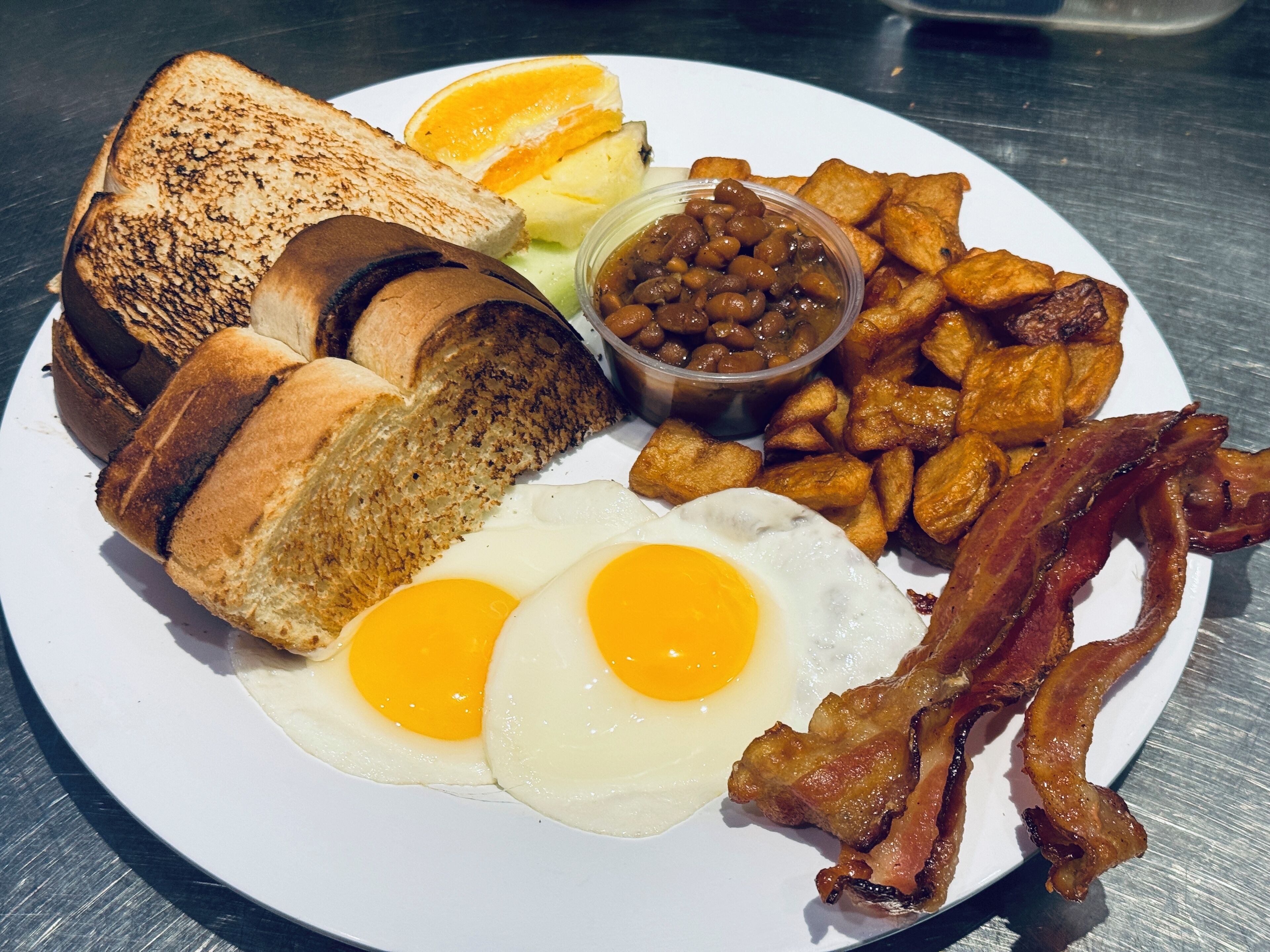 Un plato de desayuno con tostadas, huevos, tocino, frijoles y papas fritas.