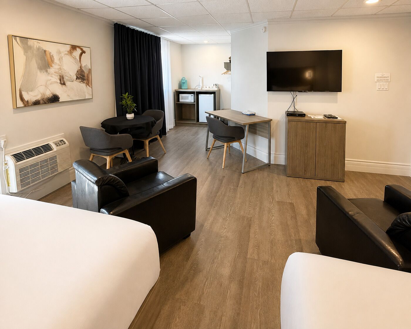A hotel room with a bed, two sofas, a desk, a television, and a large painting on the wall.