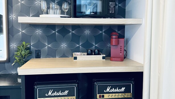 Una zona de cocina con microondas, dos amplificadores Marshall, cafetera y objetos decorativos en estantes.