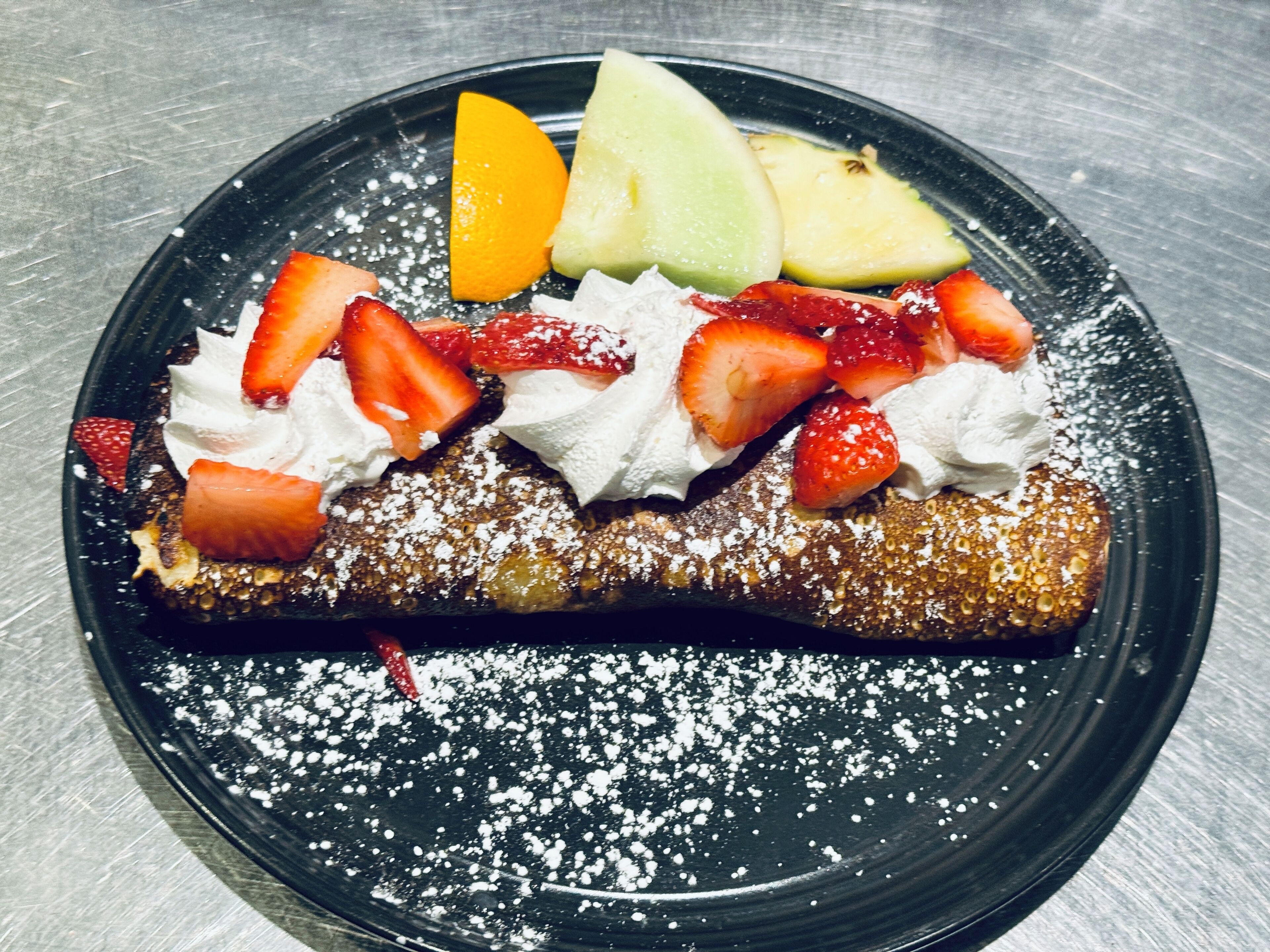 Ein Dessertteller mit einer Crêpe, Erdbeeren und einem Melonenscheibchen.