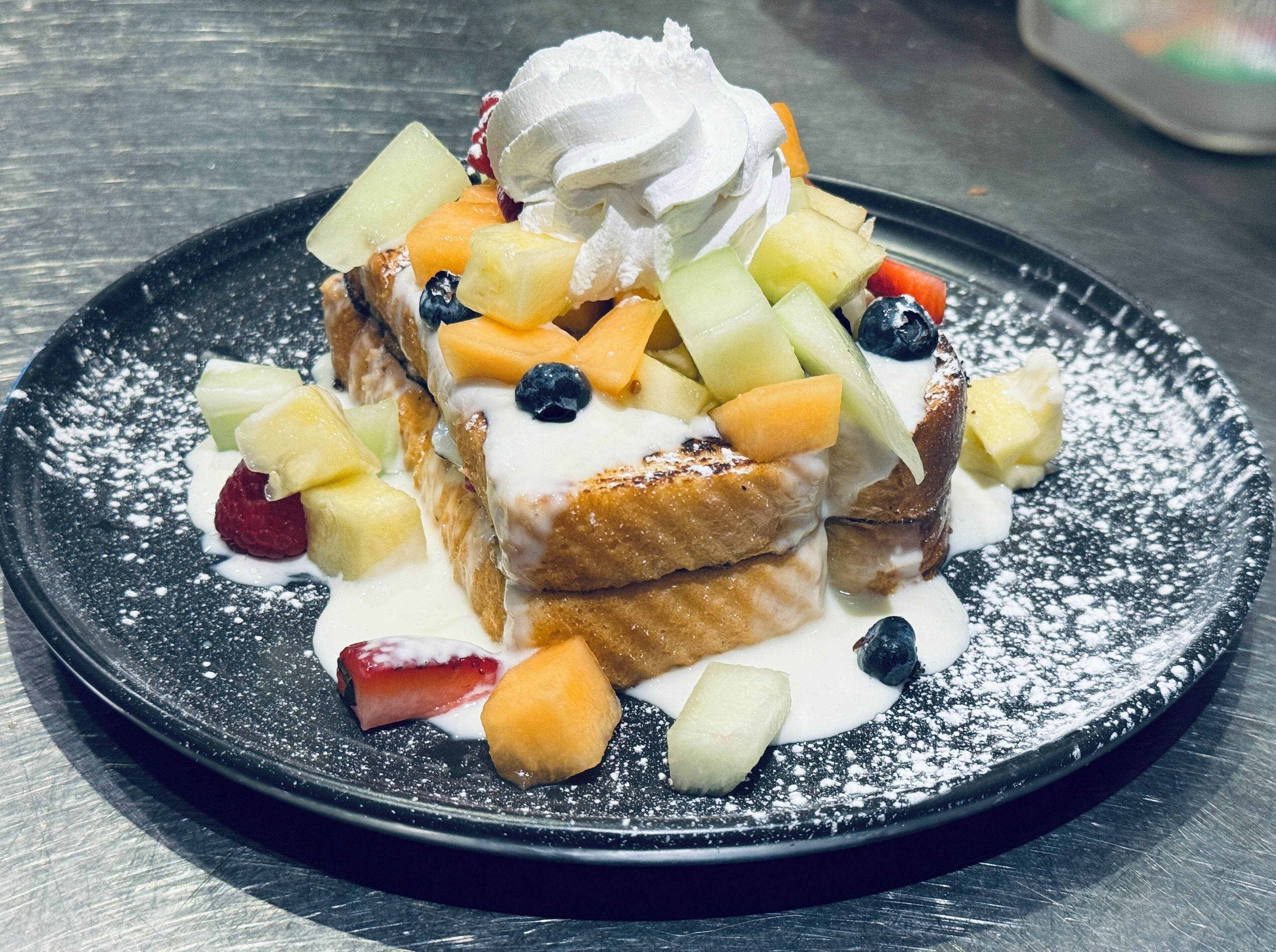 A dessert plate with fruit and whipped cream on a black plate.