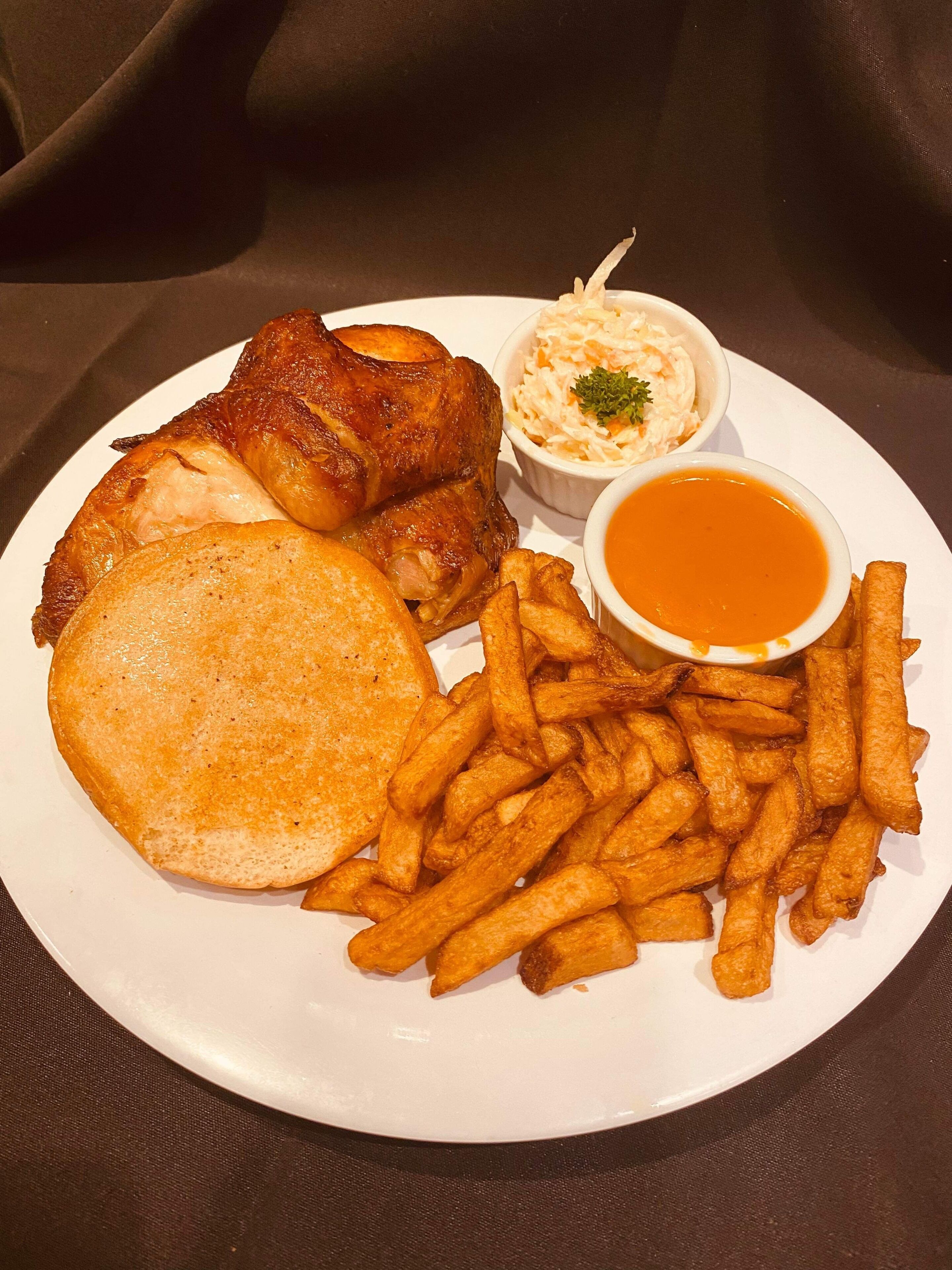 Un plato con pollo a la plancha, papas fritas, un sándwich a la parrilla y dos salsas para mojar.