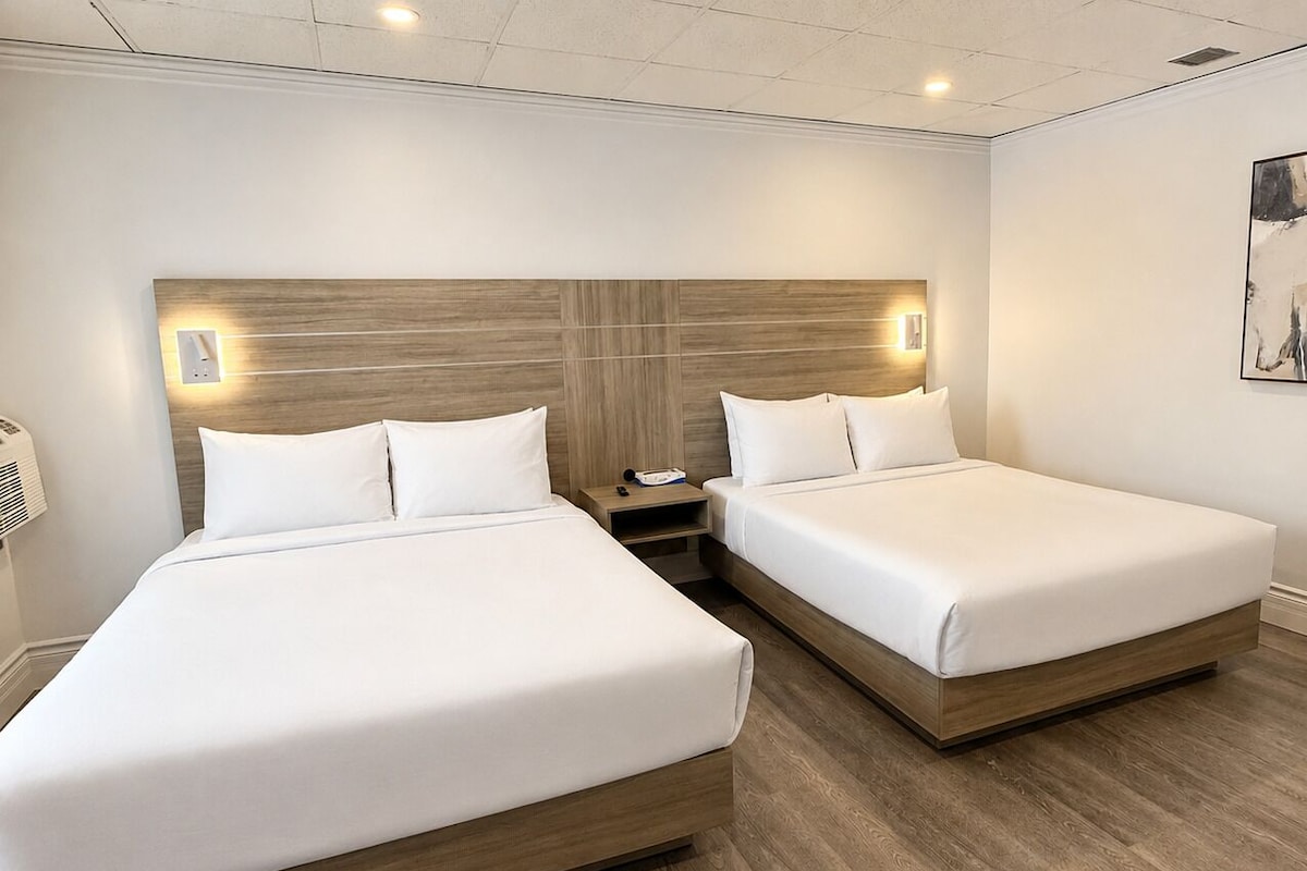 Habitación de hotel con dos camas, cabecera de madera, mesitas de noche y una lámpara de pared.