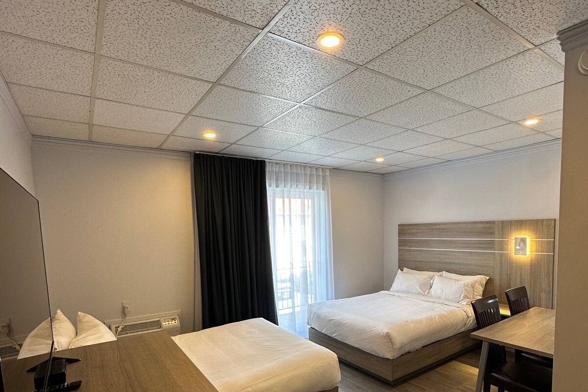 Una habitación de hotel con dos camas, un escritorio de madera, un espejo y una ventana con cortinas.