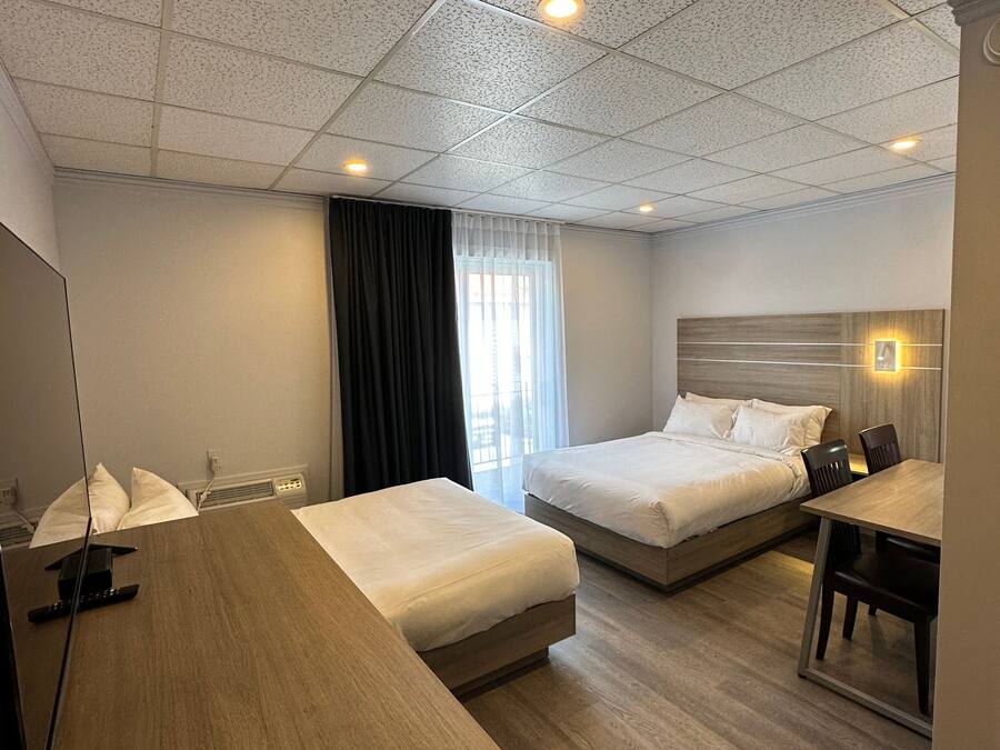 Una habitación de hotel con dos camas, un escritorio de madera, un espejo y una ventana con cortinas.
