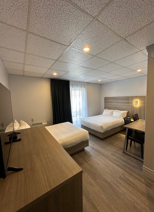Una habitación de hotel con dos camas, un escritorio de madera, un espejo y una ventana con cortinas.