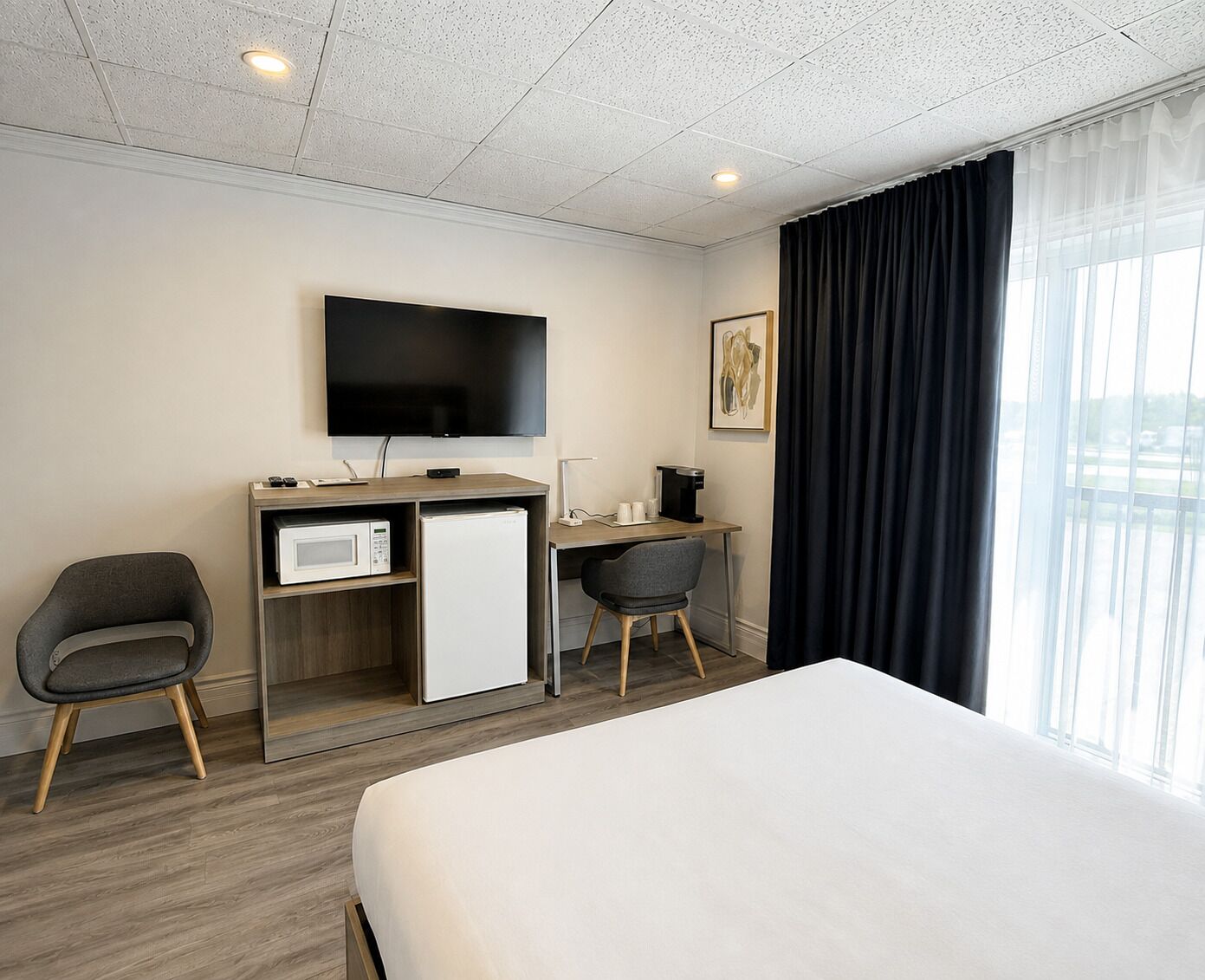 A hotel room with a bed, a desk with a computer, a television, and a window with curtains.