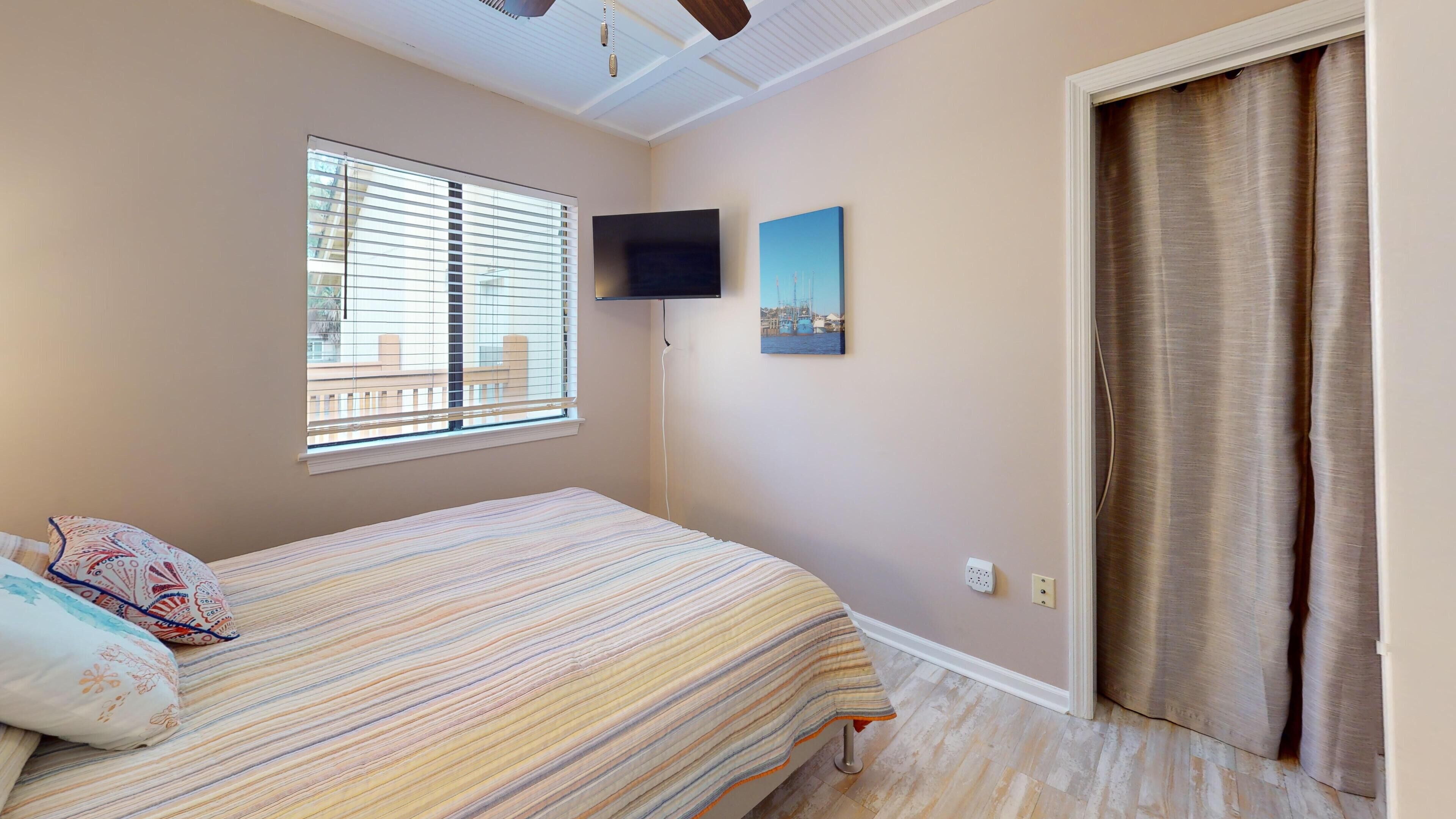 Ein Schlafzimmer mit einem Bett, einem an der Wand montierten Fernseher, einem Fenster mit Jalousien und einer Tür.