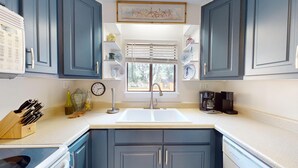 A kitchen with blue cabinets, a white sink, a coffee maker, and a window with blinds. - 2BR/2BA Condo with golf views ~ Edisto On My Mind (Edisto Island)