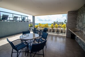 A rooftop terrace with a round table and chairs, a kitchen area, and a view of the ocean.