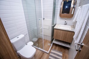 A modern bathroom with a glass-enclosed shower, a white toilet, a wooden vanity with a mirror, and a marble sink.