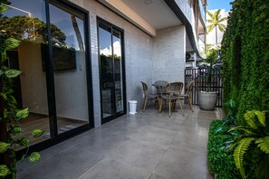 A modern patio area with a glass door leading to a balcony, a small table with chairs, and potted plants.