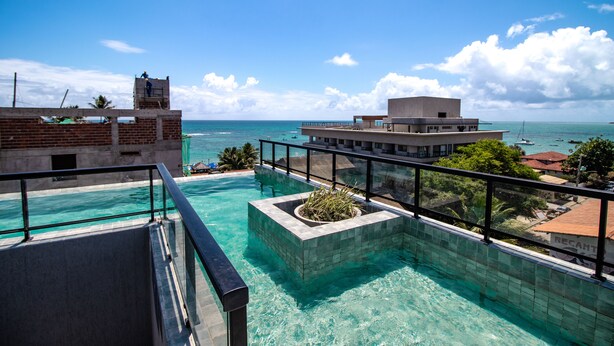A rooftop infinity pool with clear blue water, a view of the ocean, and a distant pier. - Residencial Di Mare - by New Time  (Ipojuca)