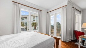 Et hotelværelse med en seng, et skrivebord, en stol og store vinduer med udsigt ud.