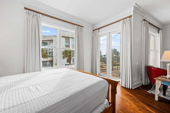 A hotel room with a bed, a desk, a chair, and large windows offering a view of the outside.