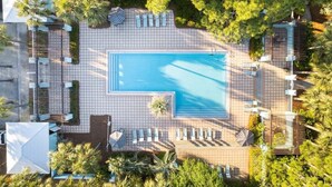 Oversigtsbillede af et resort med en central swimmingpool, omgivet af loungeområder og palmer.