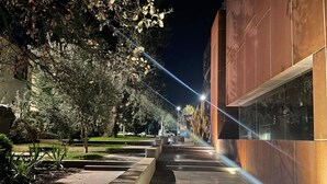 Un sendero al aire libre de noche, con un edificio moderno a la derecha, una estatua en la distancia y árboles a la izquierda.