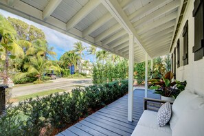 Eine überdachte Veranda mit Holzterrasse, einer weißen gepolsterten Bank und einem Blumentopf.