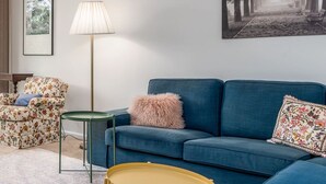 Una sala de estar con un sofá azul, un sillón estampado, una mesita redonda y una lámpara de pie.