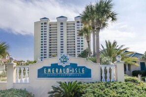 A sign for Emerald Isle Resort Condominiums with a modern building and palm trees in the background.