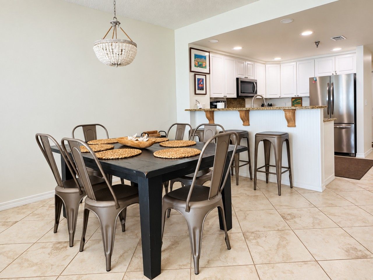 A modern kitchen with a dining area, featuring a central island, stainless steel appliances, and a chandelier.