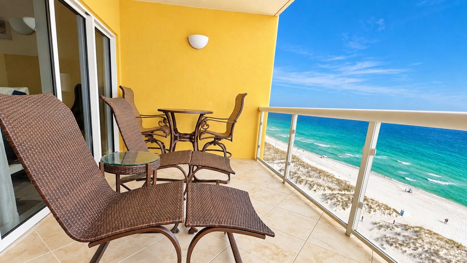 Un balcón con mobiliario de mimbre y una mesa de vidrio con vista a la playa.