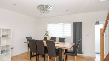 Un comedor con mesa de madera y sillas negras, una estantería blanca y una ventana con persianas.