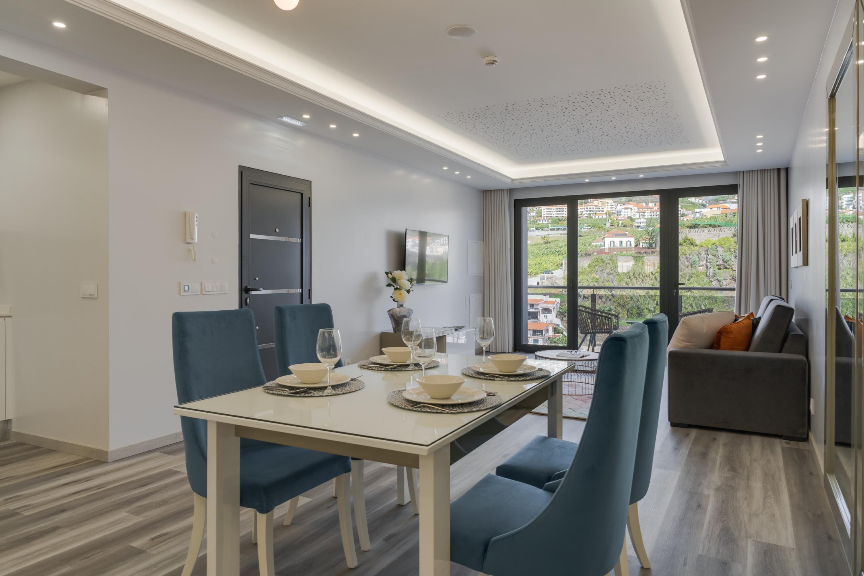 A modern dining area with a table set for four, a sofa, and a view of the city.