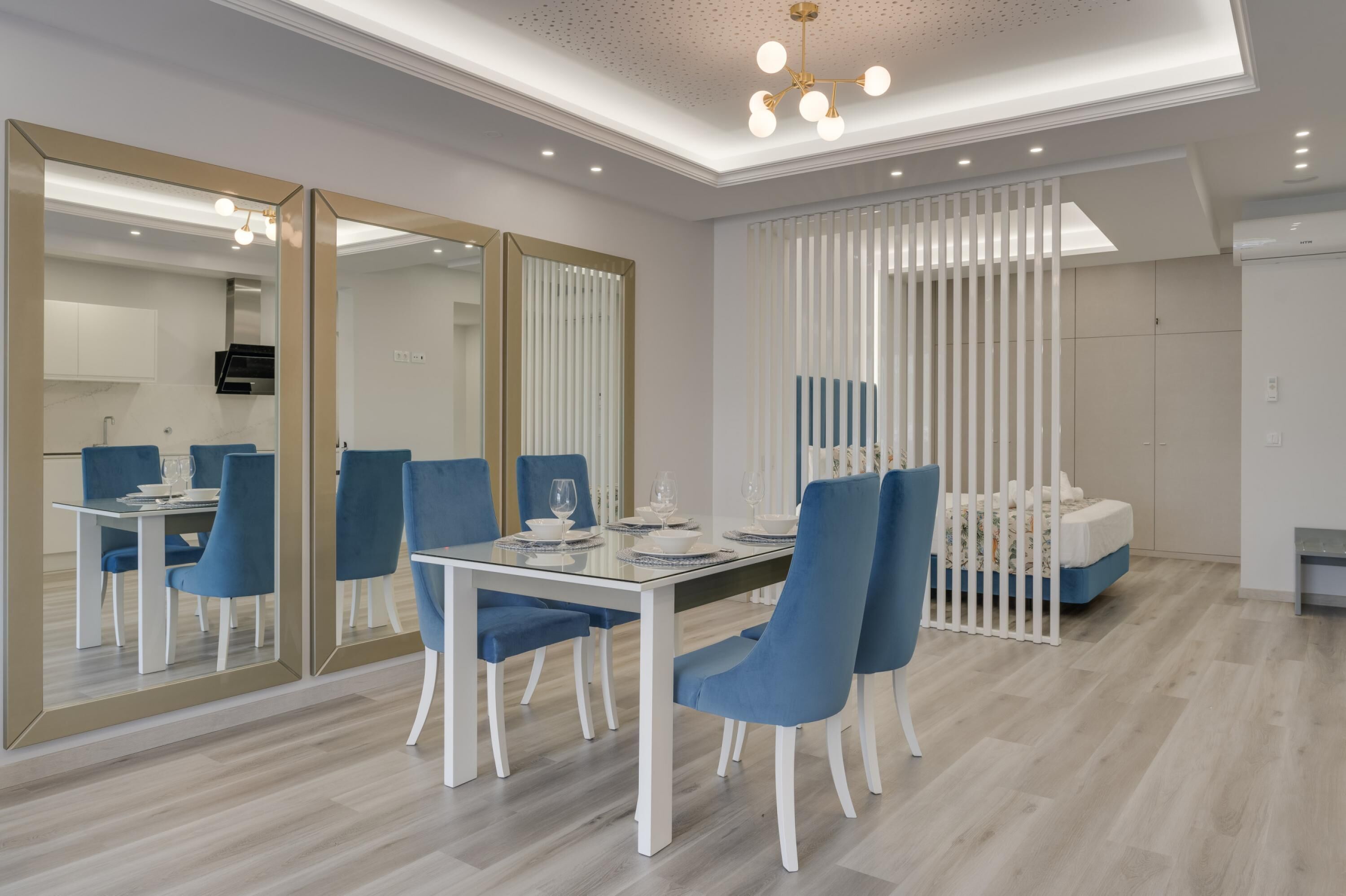 A modern dining area with a glass table, blue chairs, and a mirrored wall.