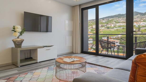 A modern living room with a large TV, a round coffee table, a sofa, and a balcony with a city view. - Torre Palace II by Atlantic Holiday (Camara de Lobos)