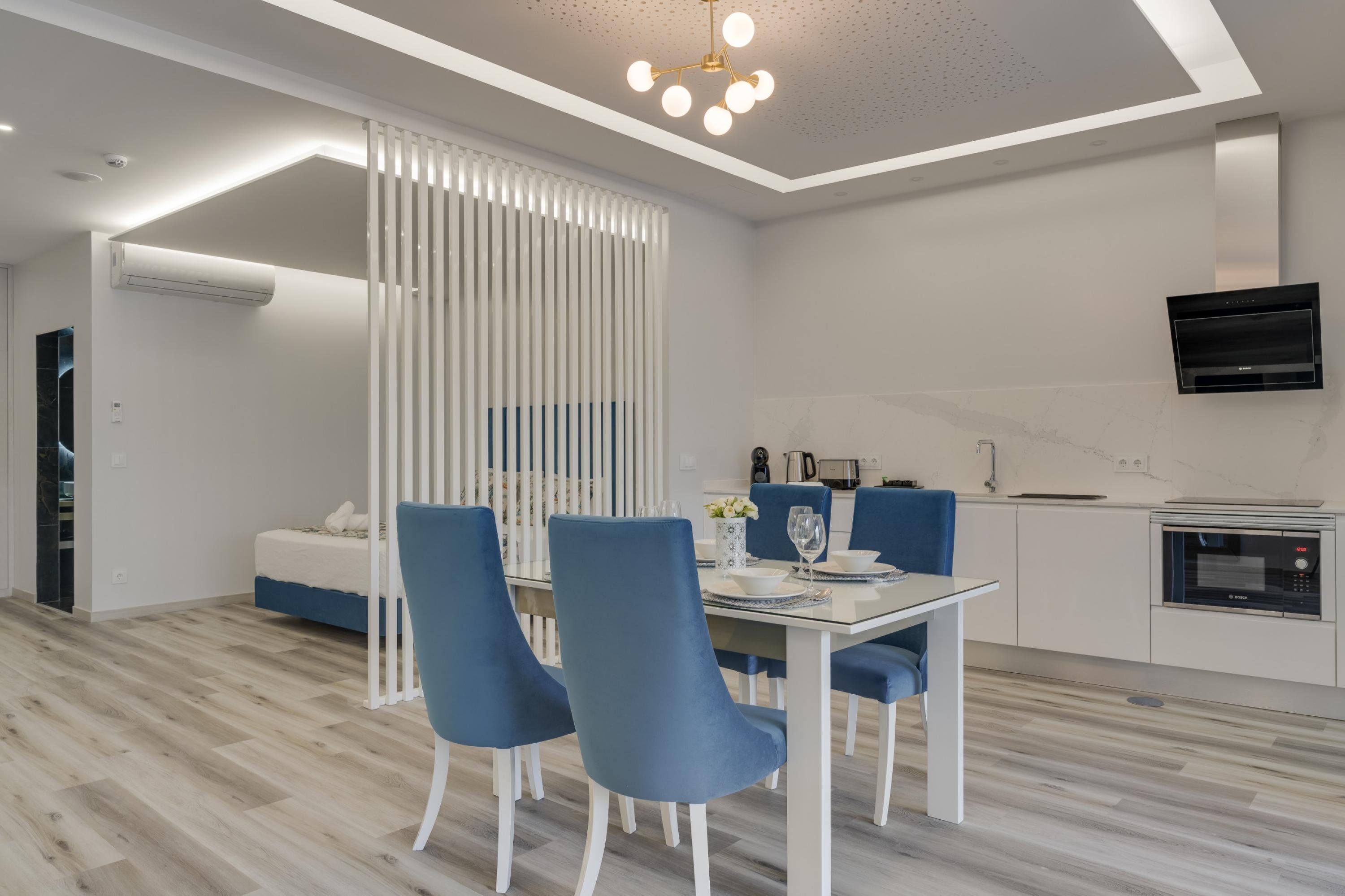 A modern living room with a dining area, a kitchen with built-in appliances, and a TV mounted on the wall.