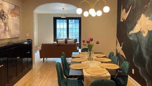 A dining area with a table set for four, surrounded by teal chairs, a chandelier, and a large painting on the wall. - Brady Street Luxury | Close to Downtown | Sleeps 8 (Milwaukee)