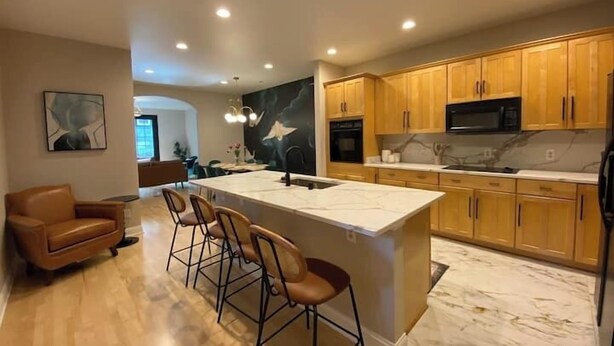 A modern kitchen with wooden cabinets, a marble countertop, and a central island with bar stools. - Brady Street Luxury | Close to Downtown | Sleeps 8 (Milwaukee)
