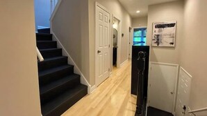 A hallway with a wooden floor, a staircase with black steps, and white doors. - Brady Street Luxury | Close to Downtown | Sleeps 8 (Milwaukee)
