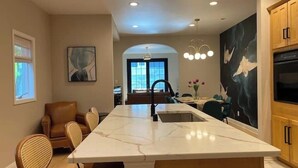 A modern kitchen with a marble island, wooden cabinets, and a dining area with a view to the outdoors. - Brady Street Luxury | Close to Downtown | Sleeps 8 (Milwaukee)