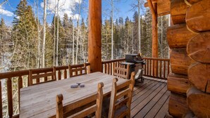 A wooden deck with a table and chairs, a grill, and a view of a forest.